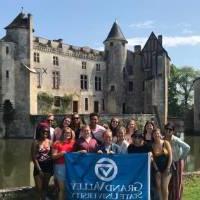 GVSU Students in front of a castle in France holding a GVSU flag